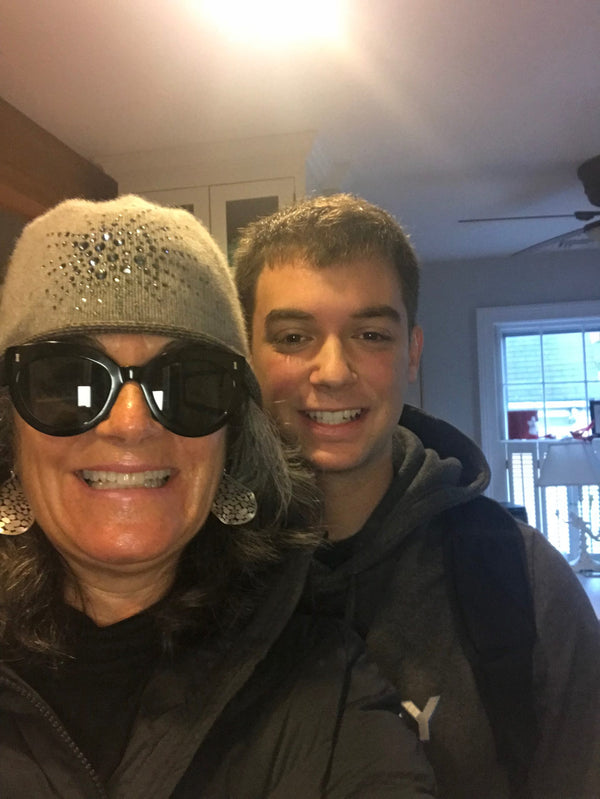 Picture of woman with long dark hair, winter hat with sparkles, big teardrop earrings and large sunglasses smiling alongside her son with short dark hair and a matching smile.