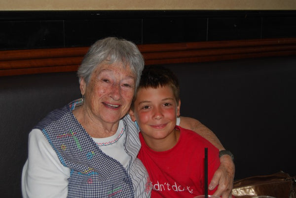 An older woman with short hair, smiling, her arm around a young boy with short hair, leaning into her, smiling.