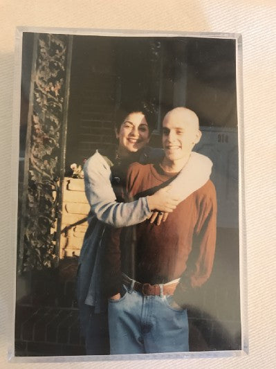 Picture of a photograph, a woman standing behind a man with her arms wrapped around him, both smiling.