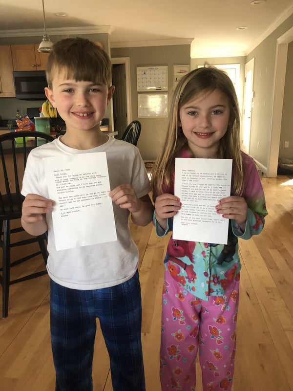 Two young kids, a boy and a girl, in their pajamas, smiling, each holding a piece of paper with a typewritten note.