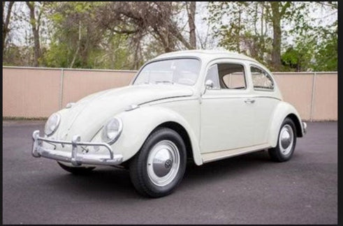 Old model of a volkswagon bug, parked in a driveway.