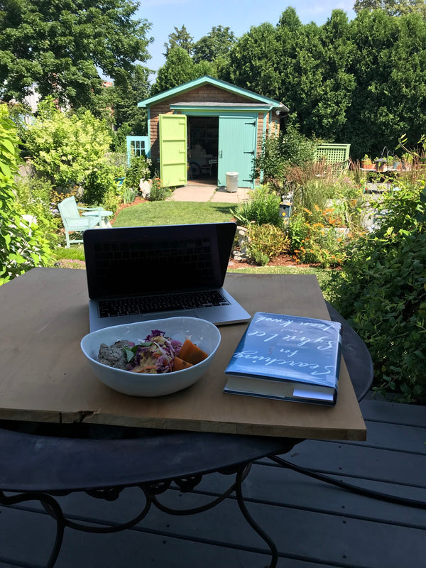 Outside, a table with a laptop, a book, and a salad. A garden in the backdrop.