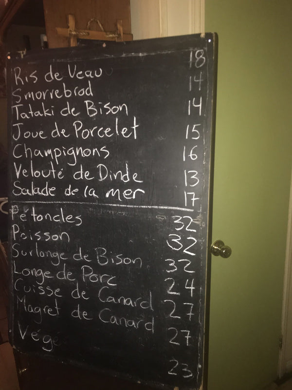 A standing chalkboard leaning against a wall with french dishes and their prices.