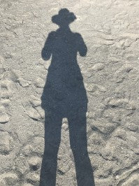 Picture of a persons shadow in the sand wearing a sunhat.