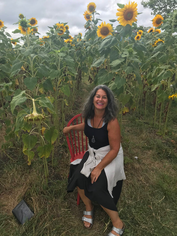 A woman sitting on a wooden chair in the middle of a sunflower field, candidly laughing.