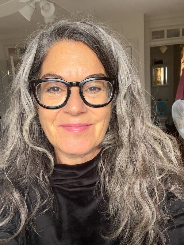 Woman with gray hair and glasses wearing a black top indoors.